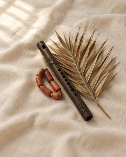 A carved wooden oja flute with coral beads and a palm frond